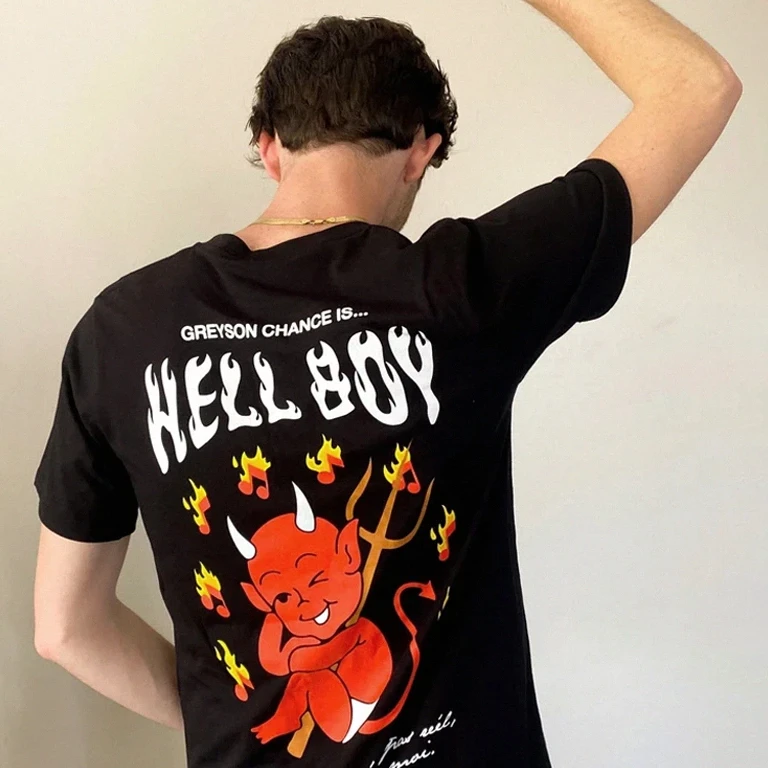 Model wearing a black Greyson Chance Hellboy T-shirt with flame typography and an illustrated red devil graphic.